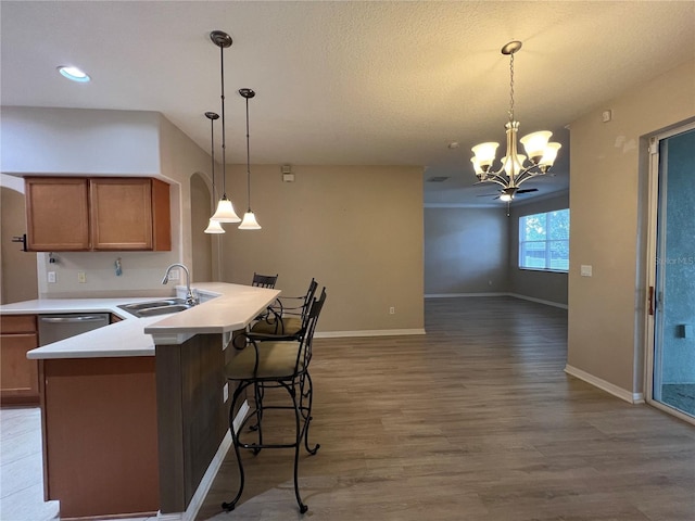 kitchen with brown cabinetry, baseboards, light wood-type flooring, a sink, and a notable chandelier