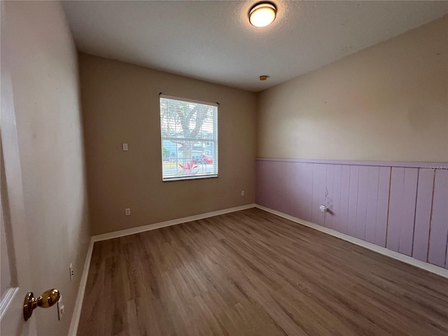 spare room featuring baseboards, wainscoting, and wood finished floors