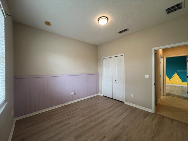 unfurnished bedroom featuring visible vents, wood finished floors, and a wainscoted wall