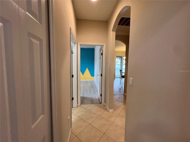 hallway featuring arched walkways and light tile patterned floors