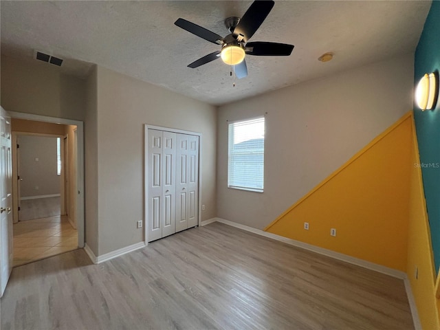 unfurnished bedroom with a textured ceiling, visible vents, light wood-type flooring, baseboards, and a closet