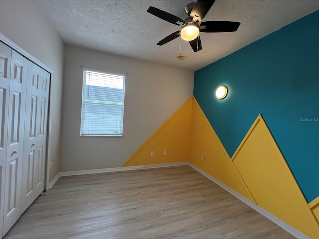 unfurnished bedroom featuring ceiling fan, a textured ceiling, baseboards, light wood-type flooring, and a closet