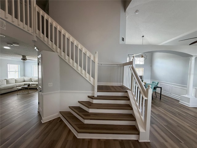 stairs with a healthy amount of sunlight, ornate columns, and wood finished floors