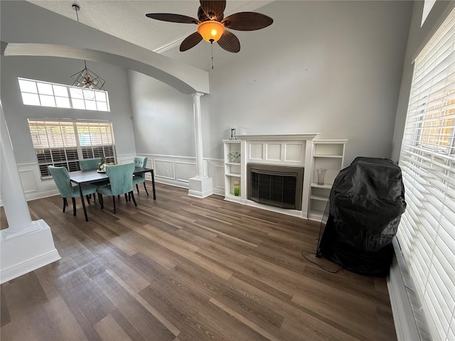 living room with a ceiling fan, a fireplace, wood finished floors, a wainscoted wall, and ornate columns