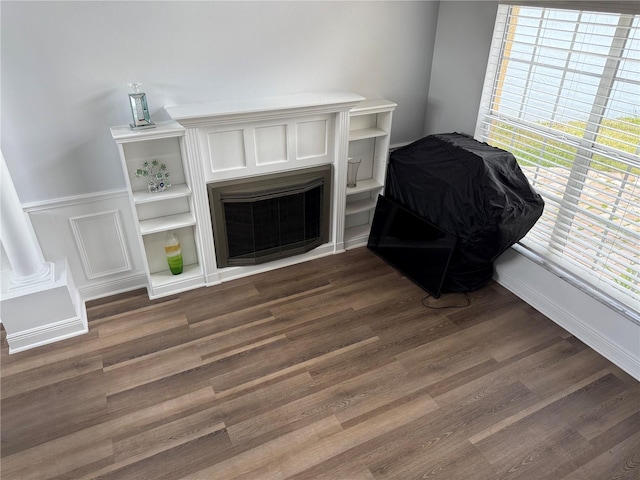 living area featuring decorative columns, wainscoting, dark wood-style floors, and a fireplace