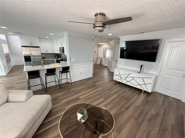 living room featuring a ceiling fan, a textured ceiling, dark wood finished floors, ornamental molding, and a decorative wall