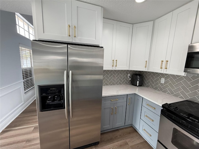 kitchen featuring gray cabinets, backsplash, light wood-style floors, stainless steel appliances, and white cabinetry