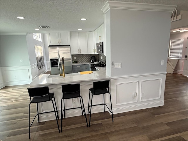 kitchen featuring visible vents, ornamental molding, a peninsula, light wood-style flooring, and appliances with stainless steel finishes