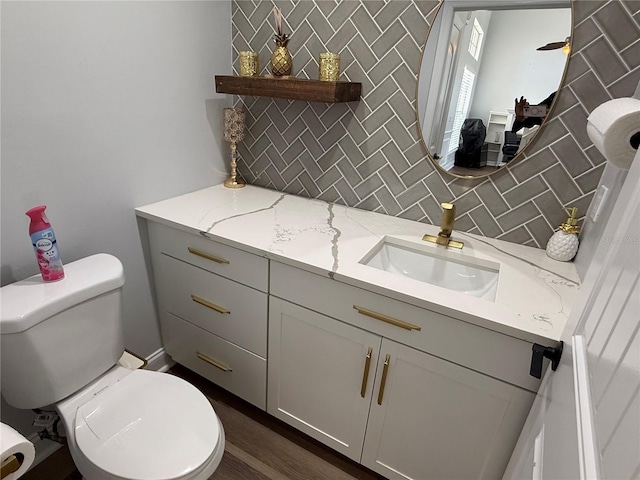 half bathroom featuring toilet, decorative backsplash, wood finished floors, and vanity
