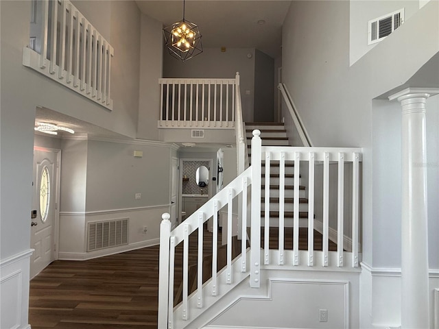 staircase featuring visible vents, a towering ceiling, wood finished floors, and a chandelier