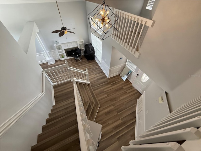 stairs with a high ceiling, a fireplace, ceiling fan with notable chandelier, and wood finished floors