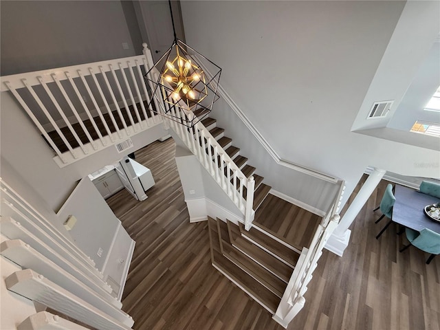 stairs with an inviting chandelier, baseboards, wood finished floors, and visible vents
