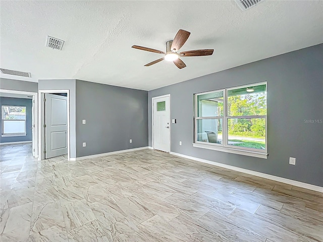 unfurnished room with a textured ceiling, a wealth of natural light, ceiling fan, and visible vents