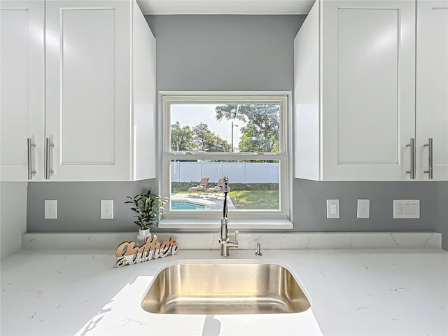kitchen with white cabinets, light stone counters, and a sink
