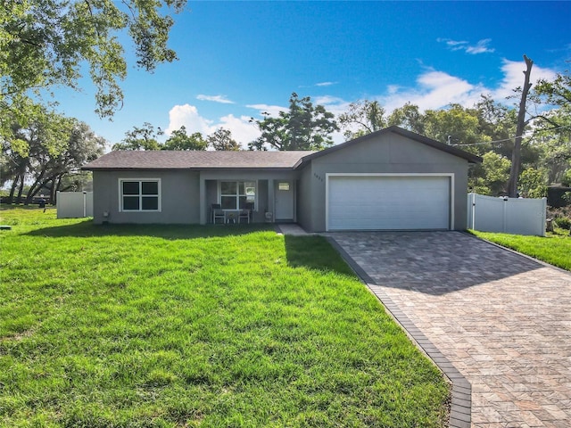 ranch-style house with fence, an attached garage, stucco siding, a front yard, and decorative driveway