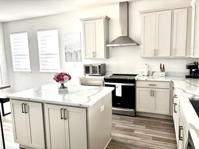 kitchen featuring stainless steel electric range, light stone counters, light wood-style floors, wall chimney exhaust hood, and a kitchen island