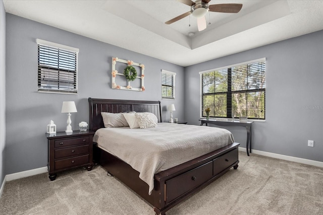 bedroom with a ceiling fan, baseboards, light carpet, and a tray ceiling