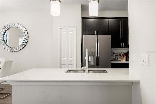 kitchen with stainless steel fridge, a sink, light countertops, dark cabinets, and wood finished floors