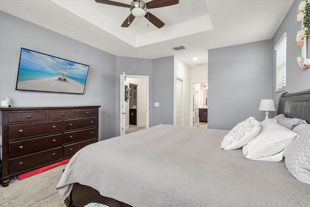 carpeted bedroom featuring ceiling fan, a tray ceiling, connected bathroom, and visible vents