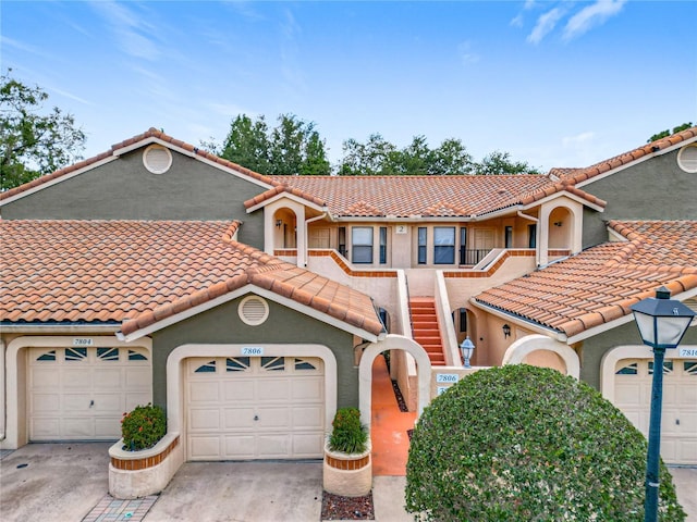 mediterranean / spanish-style house with a garage, stucco siding, a tiled roof, and concrete driveway