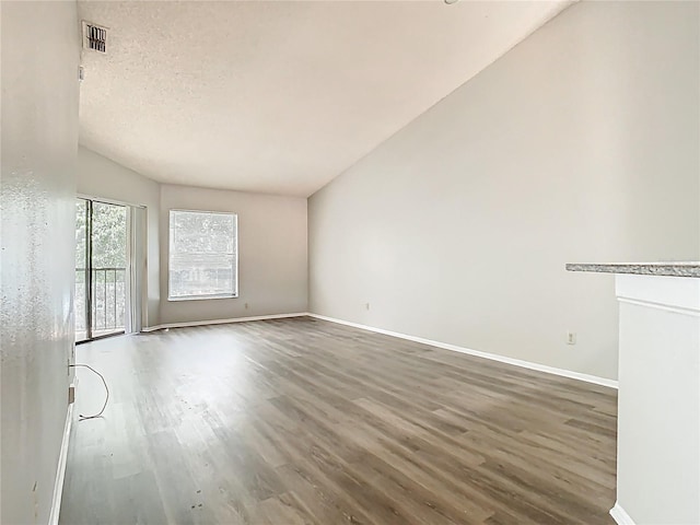 empty room featuring baseboards, visible vents, wood finished floors, and lofted ceiling