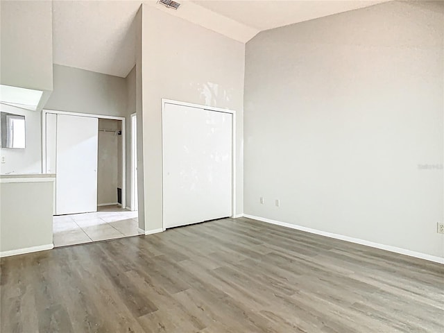 unfurnished bedroom featuring high vaulted ceiling, multiple closets, baseboards, wood finished floors, and visible vents