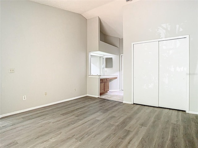 unfurnished bedroom with baseboards, light wood finished floors, vaulted ceiling, and a closet