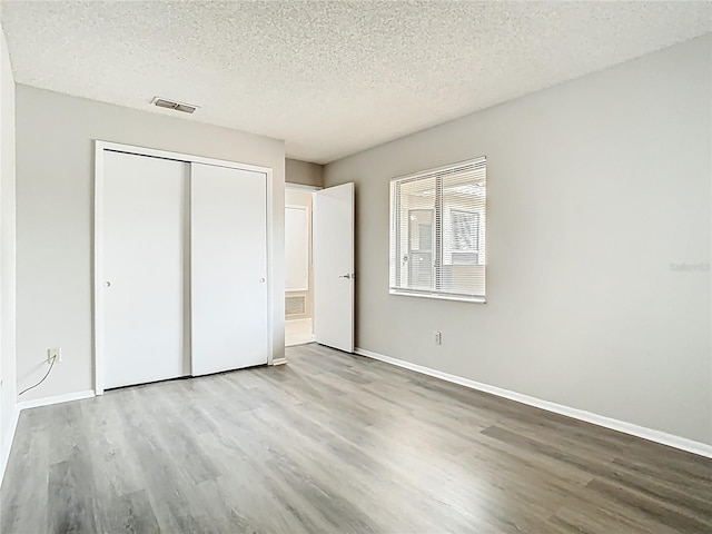 unfurnished bedroom with visible vents, a textured ceiling, wood finished floors, and a closet
