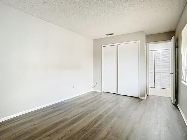 unfurnished bedroom with a textured ceiling, visible vents, wood finished floors, baseboards, and a closet