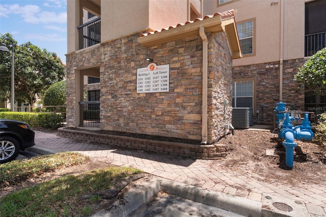 view of side of property with central air condition unit, stucco siding, a balcony, and stone siding