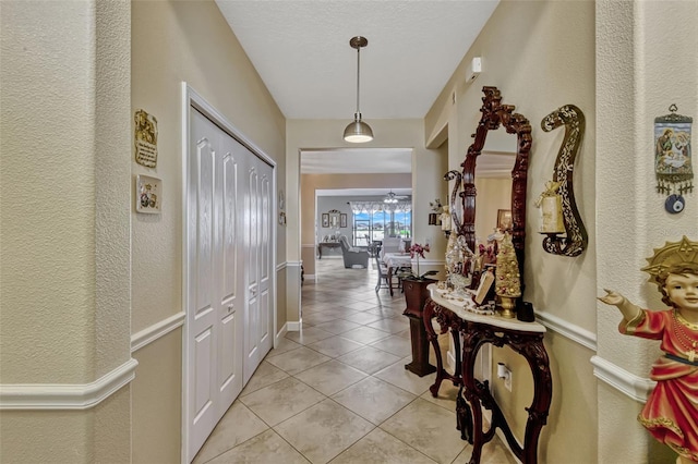 hallway featuring baseboards, a textured wall, and light tile patterned floors