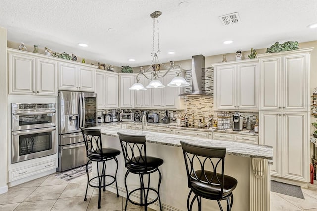 kitchen featuring visible vents, a breakfast bar, wall chimney exhaust hood, appliances with stainless steel finishes, and decorative light fixtures
