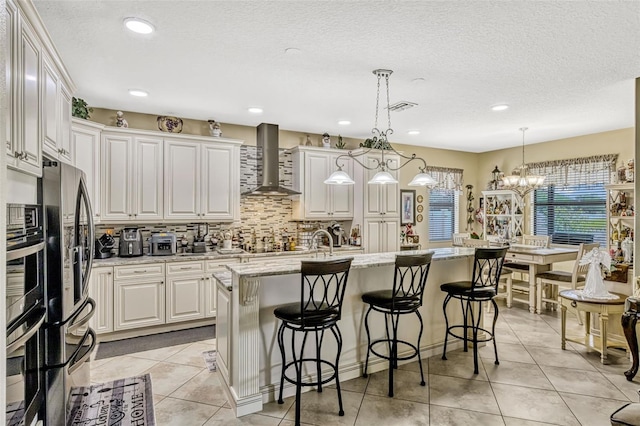 kitchen with light tile patterned flooring, wall chimney exhaust hood, stainless steel appliances, decorative backsplash, and a kitchen bar