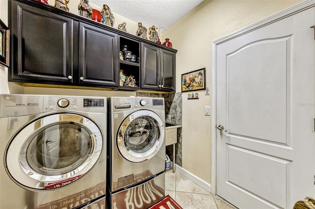 washroom with a textured ceiling, washing machine and clothes dryer, cabinet space, light tile patterned floors, and baseboards