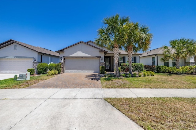 ranch-style home with a garage, decorative driveway, stucco siding, and a front yard