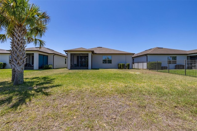 rear view of property featuring a lawn, fence, stucco siding, and a sunroom