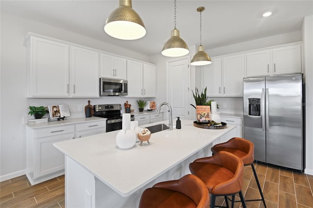 kitchen with a sink, appliances with stainless steel finishes, wood finish floors, and a kitchen bar
