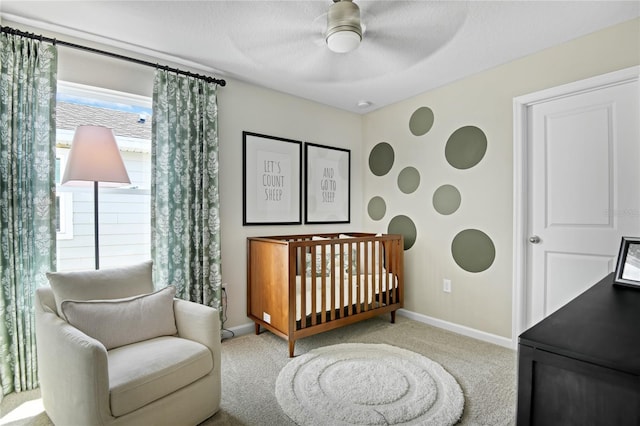 carpeted bedroom featuring a crib, baseboards, and a ceiling fan