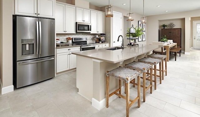kitchen with appliances with stainless steel finishes, tasteful backsplash, a sink, a breakfast bar, and an island with sink