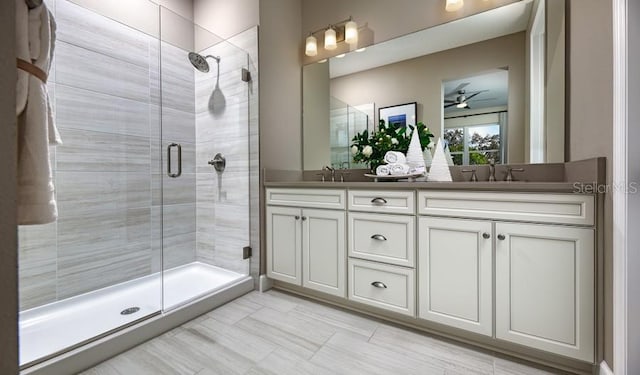 full bath with double vanity, a sink, ceiling fan, and a shower stall