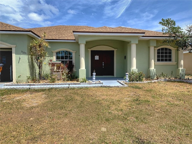 entrance to property featuring a yard, roof with shingles, and stucco siding