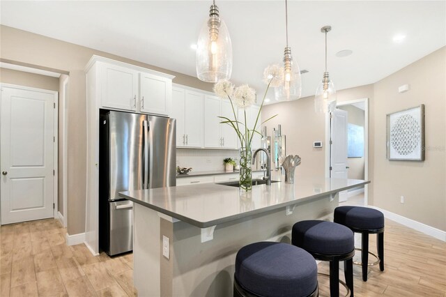 kitchen with freestanding refrigerator, a kitchen island with sink, baseboards, light wood-type flooring, and a sink