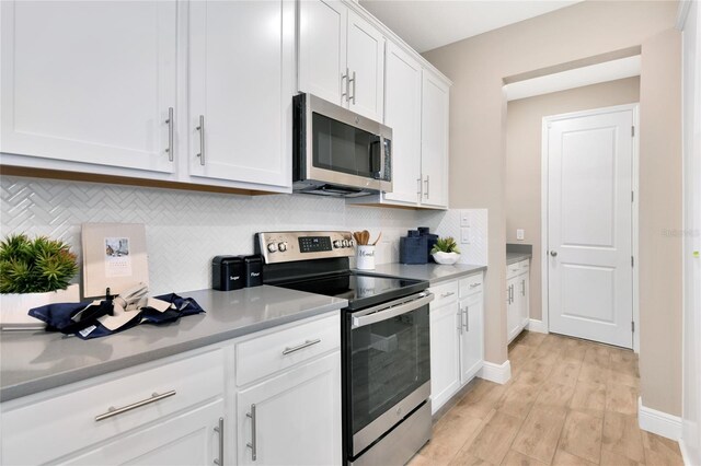 kitchen featuring tasteful backsplash, baseboards, white cabinets, light wood-style floors, and stainless steel appliances