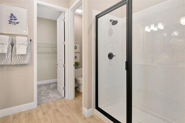 full bathroom with a walk in closet, a stall shower, wood finished floors, baseboards, and toilet