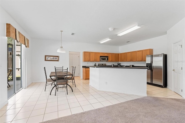 kitchen featuring brown cabinetry, pendant lighting, dark countertops, light tile patterned floors, and stainless steel appliances
