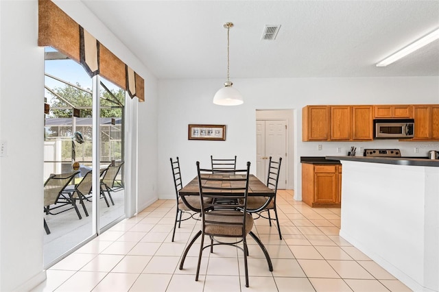 kitchen with brown cabinetry, decorative light fixtures, visible vents, dark countertops, and stainless steel microwave