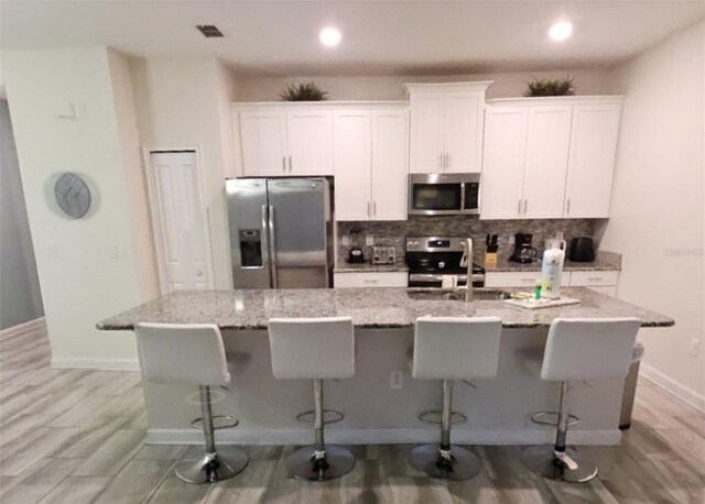 9079 Dogleg Dr, Davenport, FL 33896 - kitchen with appliances with stainless steel finishes, a kitchen island with sink, white cabinets, tasteful backsplash, and recessed lighting