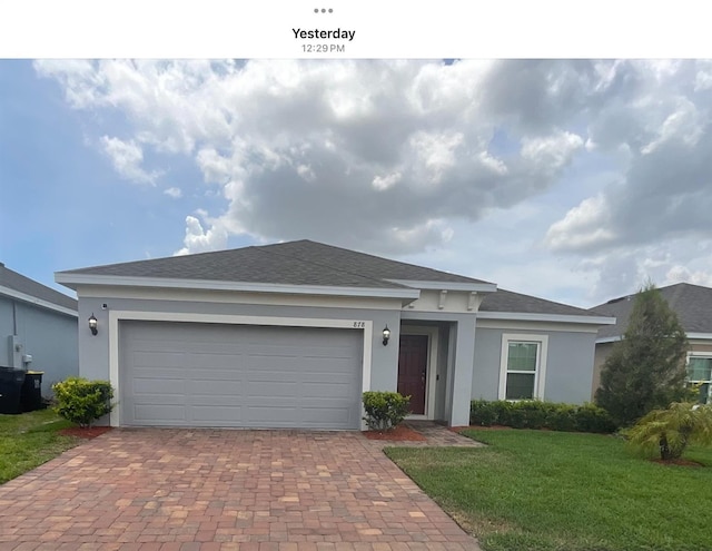 view of front of property with decorative driveway, a garage, stucco siding, roof with shingles, and a front lawn