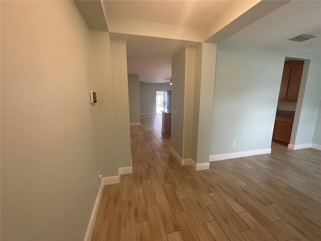 corridor featuring light wood-style flooring, baseboards, and visible vents