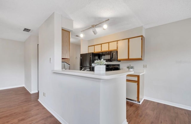 kitchen featuring light countertops, black appliances, wood finished floors, and visible vents